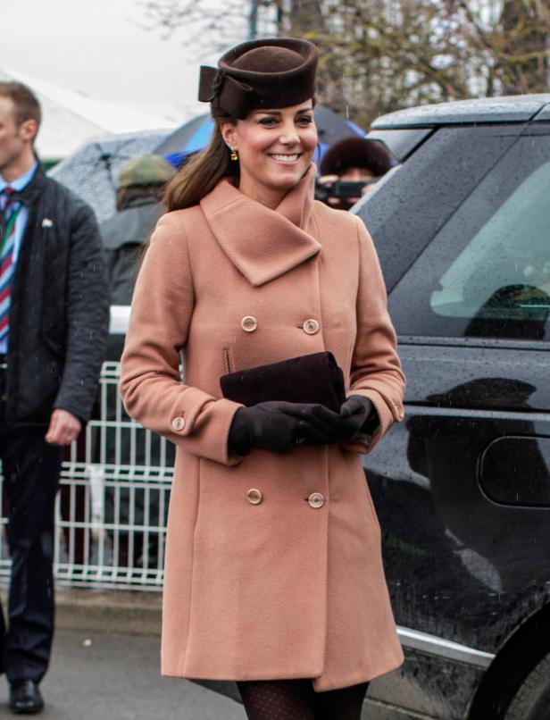 Kate Middleton lächelt in einem rosa Mantel und braunem Hut.