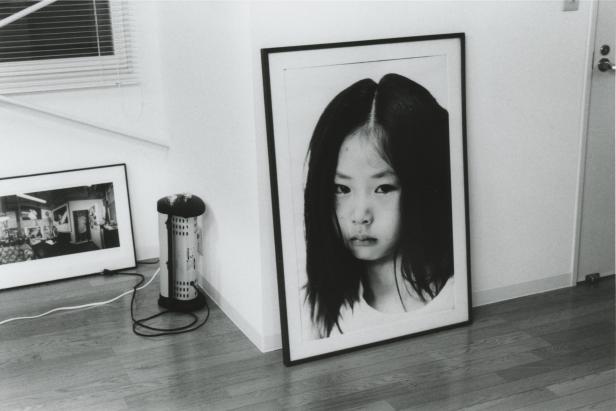 Ein gerahmtes Schwarz-Weiß-Porträt eines jungen Mädchens steht auf einem Holzboden.