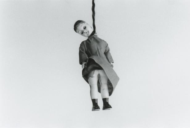 Eine Puppe mit einem Mantel hängt an einem dunklen Haarstrang.