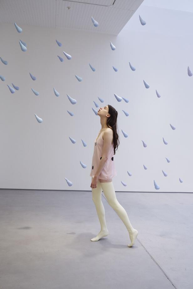 Eine Frau blickt in einem Raum mit schwebenden Regentropfen nach oben.