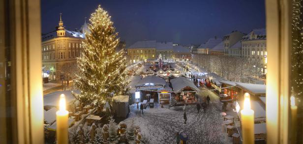 Blick aus dem Fenster auf einen verschneiten Weihnachtsmarkt mit großem Weihnachtsbaum.