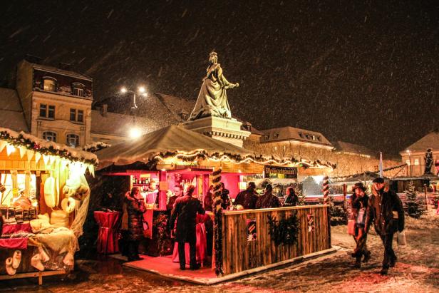 Ein Weihnachtsmarkt mit einer Statue im Hintergrund bei Schneefall.