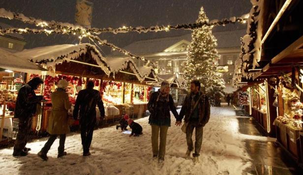 Ein verschneiter Weihnachtsmarkt mit Menschen und einem großen Weihnachtsbaum.