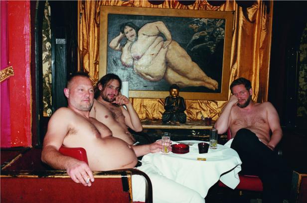 Drei Männer sitzen barfuß in einem dekadenten Raum mit einem Gemälde und einer Buddha-Statue.