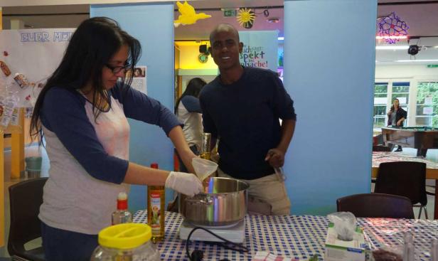 Eine Frau gießt Öl in einen Topf, während ein Mann danebensteht und lächelt.