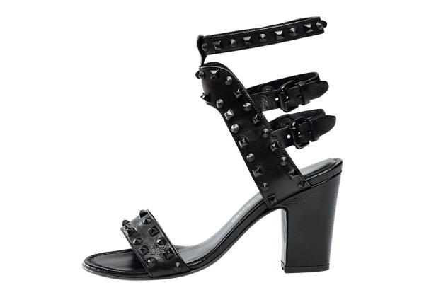 Ein schwarzer, nietenbesetzter Sandalette mit Absatz vor einem weißen Hintergrund.