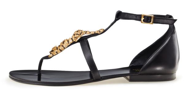 Eine schwarze Sandale mit goldenen Schmucksteinen und einem Knöchelriemen.