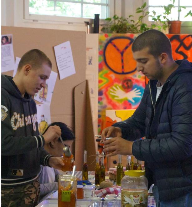 Zwei junge Männer füllen Gläser mit eingelegten Produkten an einem Tisch.