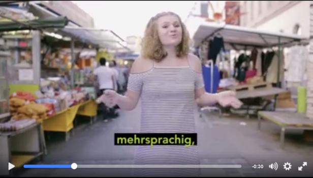 sag's multi!-video-aufruf Eine Frau steht auf einem belebten Markt und gestikuliert.
