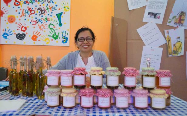 Eine Frau lächelt hinter einem Tisch mit selbstgemachten Marmeladen und Ölflaschen.