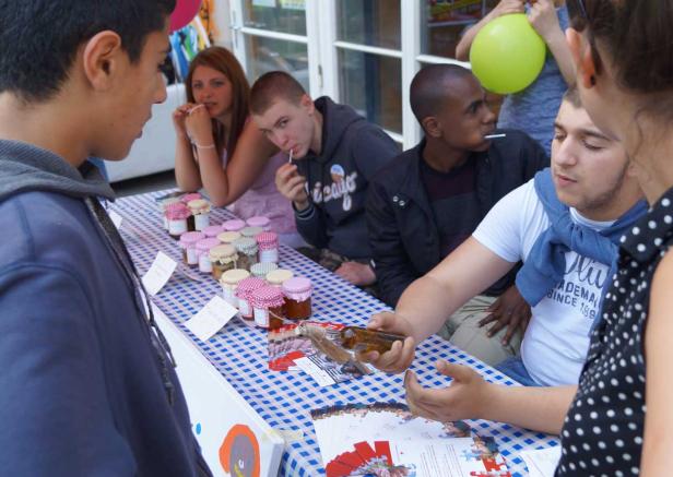 Eine Gruppe junger Leute steht an einem Stand mit Marmeladengläsern.