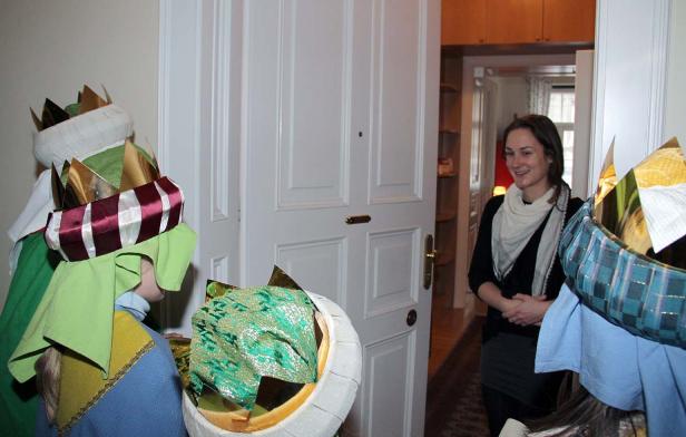 Sternsinger stehen vor einer Haustür, wo eine Frau sie freundlich empfängt.