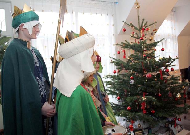 Kinder, verkleidet als die Heiligen Drei Könige, stehen neben einem Weihnachtsbaum.