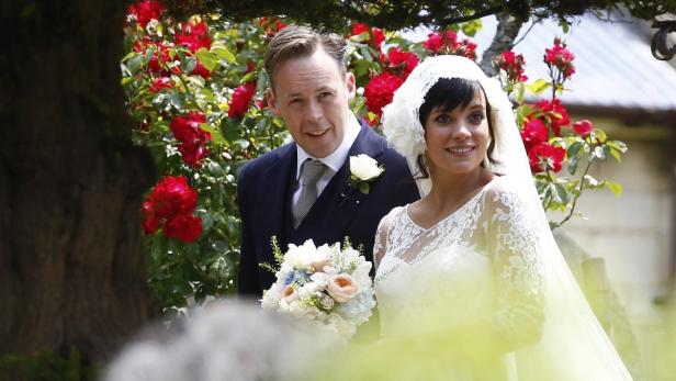 Lily Allen und David Harbour an ihrem Hochzeitstag vor einem Hintergrund aus roten Rosen.