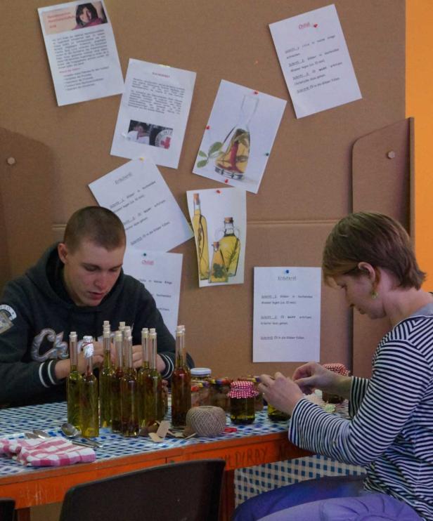 Zwei Personen sitzen an einem Tisch und bereiten Kräuteröl und Chiliöl zu.