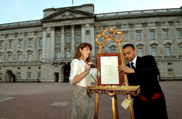 Eine Frau und ein Mann präsentieren eine Urkunde vor dem Buckingham Palace.