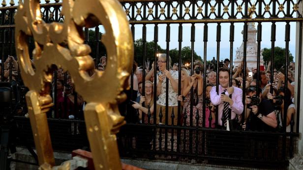 Menschen stehen hinter einem Zaun und fotografieren den Buckingham Palace.