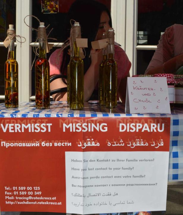 Auf einem Tisch stehen Flaschen mit Kräuter- und Chiliöl neben einem Vermissten-Hinweis des Roten Kreuzes.