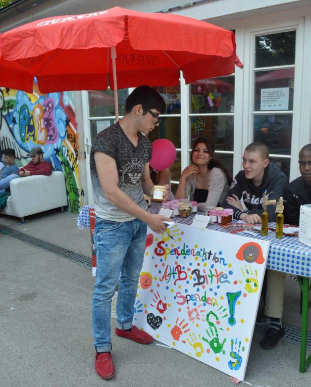Ein junger Mann steht vor einem Stand mit einem Schild, das zu Spenden aufruft.