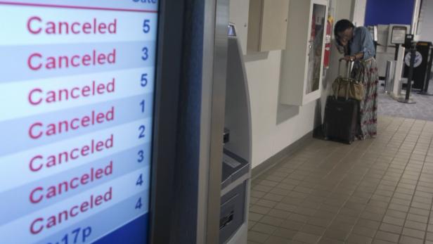 Eine Frau telefoniert neben einer Anzeigetafel mit gestrichenen Flügen am Flughafen.