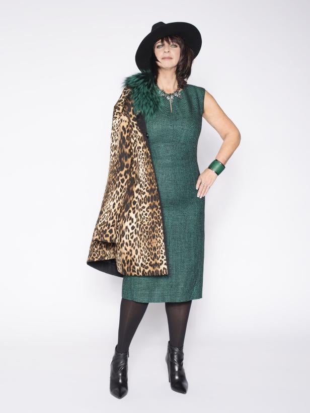 Eine Frau mit Hut und Leopardenmantel vor einem weißen Hintergrund.