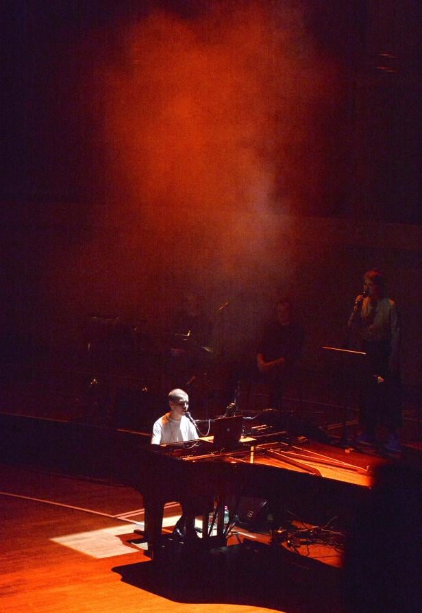 Ein Mann spielt Klavier und singt auf einer Bühne mit roter Beleuchtung.