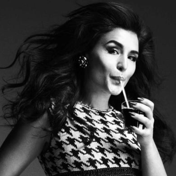 Eine Frau im Hahnentrittmuster-Top trinkt mit einem Strohhalm aus einem Glas.