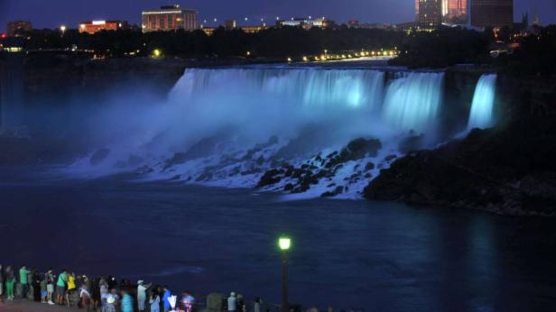 Die beleuchteten Niagarafälle bei Nacht mit Menschen im Vordergrund.