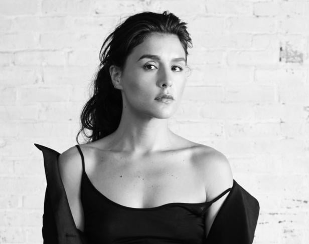 Schwarzweiß-Porträt einer Frau mit dunklen Haaren vor einer weißen Ziegelwand.