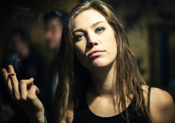 Eine Frau mit langen Haaren hält eine Zigarette in der Hand.