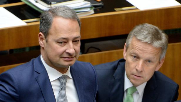 Zwei Männer in Anzügen sitzen nebeneinander.