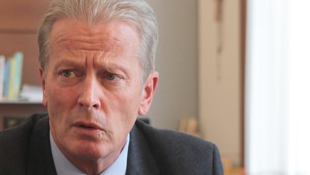 Porträt eines Mannes mit grauem Haar und einem dunklen Anzug.