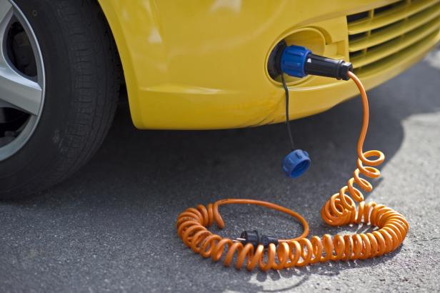 Ein gelbes Auto wird mit einem orangefarbenen Spiralkabel aufgeladen.