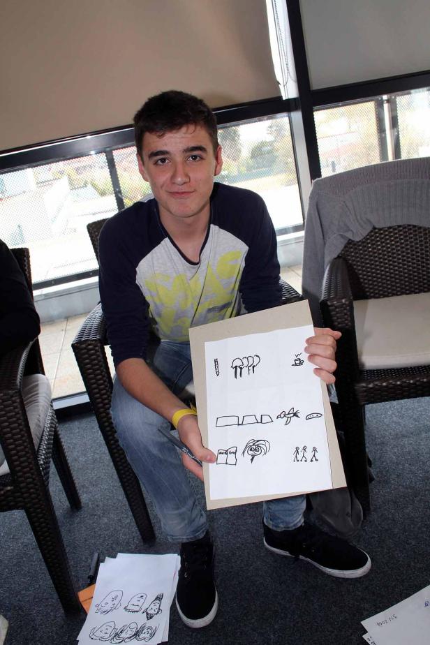 Ein junger Mann sitzt und präsentiert eine Zeichnung mit einfachen Symbolen.