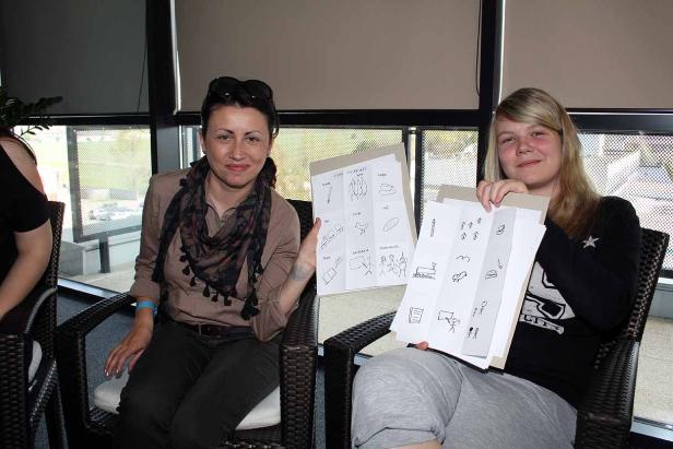 Zwei Frauen sitzen und halten Blätter mit gezeichneten Vokabeln hoch.