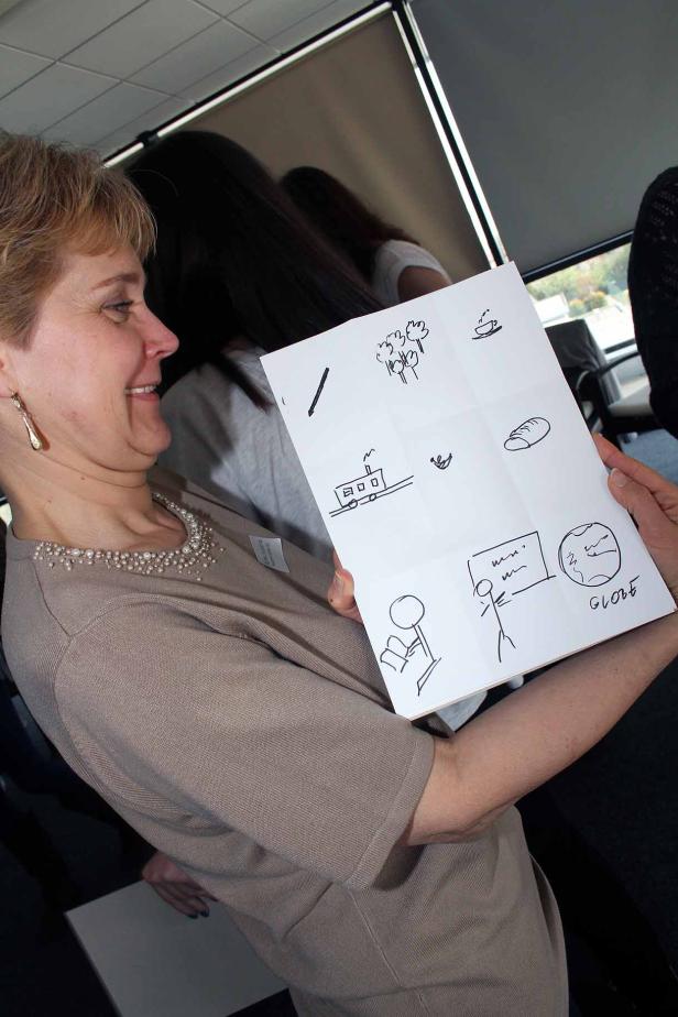 Eine Frau hält ein Blatt Papier mit einfachen Zeichnungen, darunter ein Globus und ein Zug.