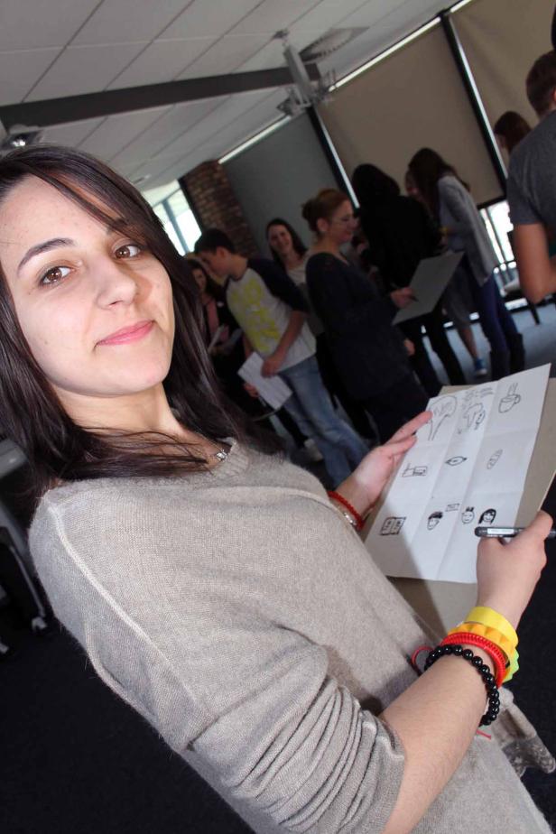 Eine junge Frau hält ein Blatt Papier mit Zeichnungen in der Hand.