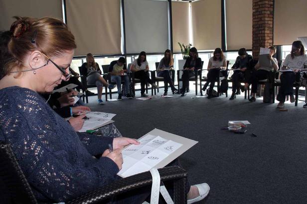 Eine Gruppe von Leuten sitzt im Kreis und zeichnet auf Papier.