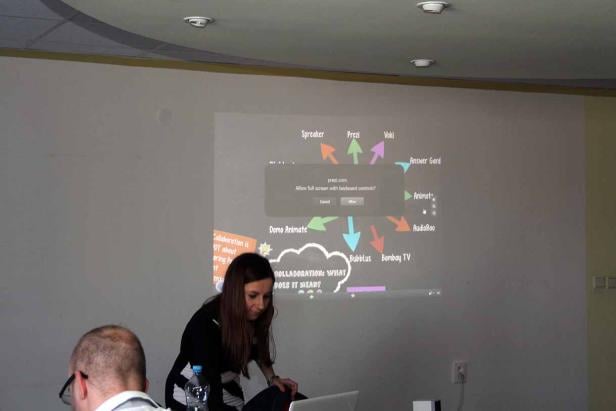 Eine Frau arbeitet an einem Laptop vor einer Präsentation über Kollaborationstools wie Prezi und Animoto.