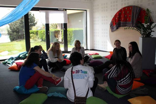 Eine Gruppe von Frauen sitzt im Kreis auf Kissen in einem hellen Raum.