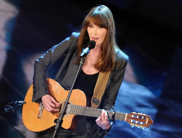 Carla Bruni singt und spielt Gitarre auf einer Bühne.