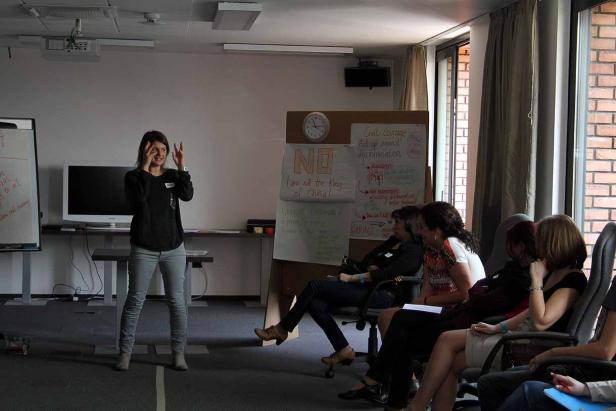 Eine Frau hält einen Vortrag vor einer Gruppe von Zuhörern in einem Konferenzraum.
