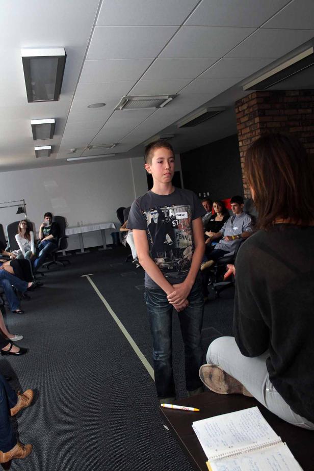 Ein Jugendlicher steht vor einer Gruppe von Menschen in einem Raum.