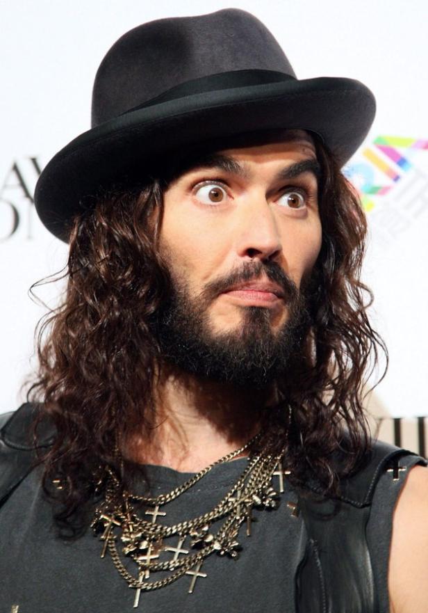 Russell Brand mit Hut und mehreren Halsketten mit Kreuzen blickt überrascht zur Seite.