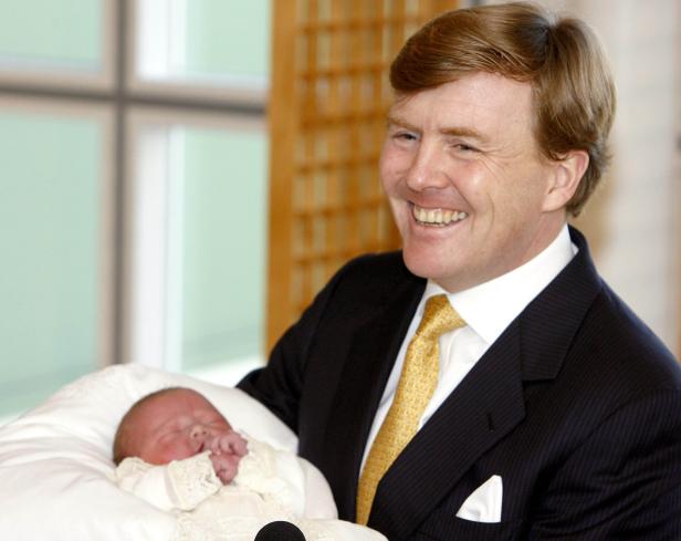 König Willem-Alexander hält ein neugeborenes Baby im Arm und lächelt.