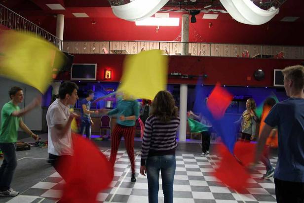 Eine Gruppe von Menschen schwingt farbige Tücher in einem Raum mit Schachbrettmuster.