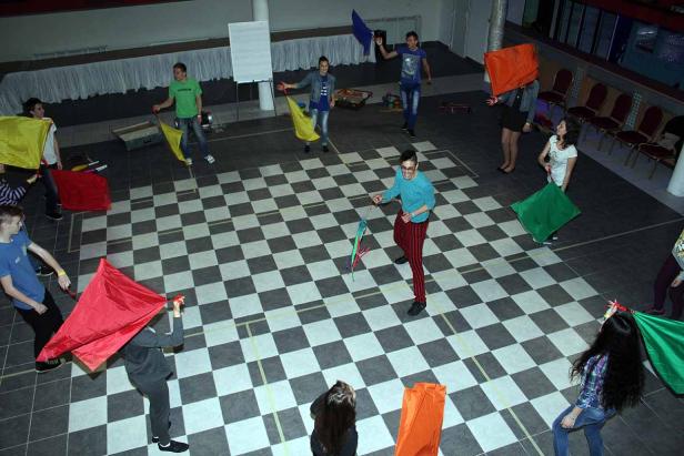 Eine Gruppe von Menschen schwingt farbige Tücher auf einem Schachbrettmusterboden.