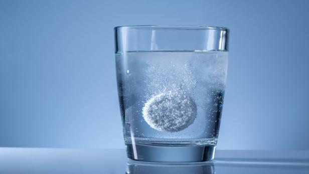 Eine Brausetablette löst sich in einem Glas Wasser auf.