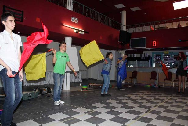 Eine Gruppe von Personen hantiert mit farbigen Tüchern in einem Raum mit Schachbrettmuster.