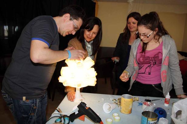 Eine Gruppe von Personen bastelt gemeinsam an einer Lampe aus recycelten Materialien.